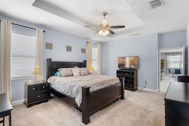 bedroom with a tray ceiling, light carpet, baseboards, and ceiling fan