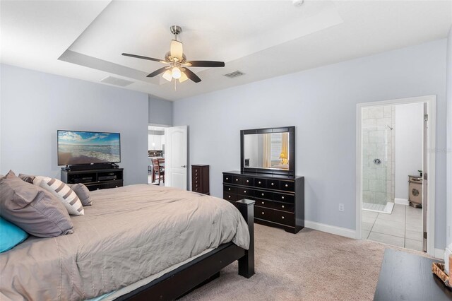 bedroom with baseboards, light carpet, connected bathroom, a raised ceiling, and a ceiling fan