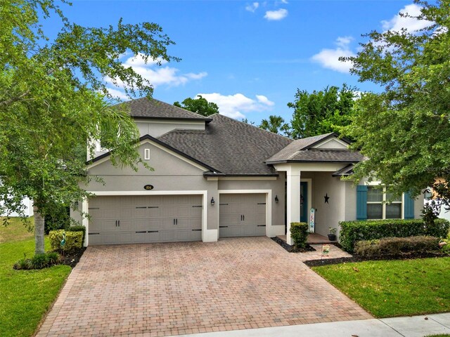 view of front of house with stucco siding, decorative driveway, an attached garage, roof with shingles, and a front lawn