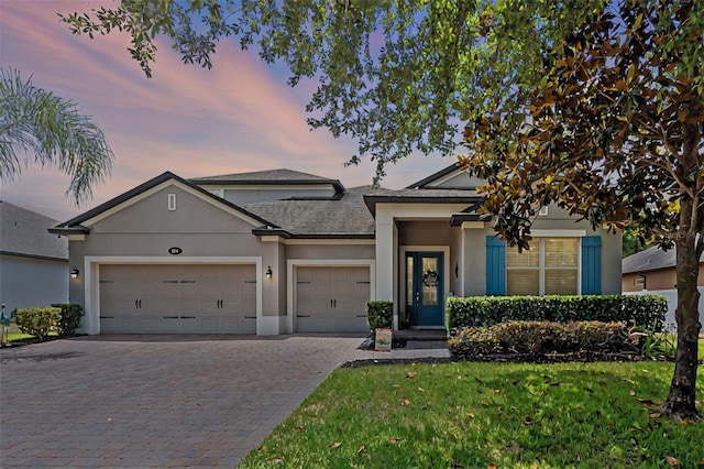 view of front of home featuring an attached garage, decorative driveway, stucco siding, a front lawn, and roof with shingles