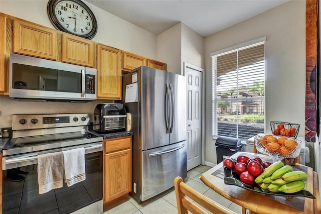 kitchen featuring dark countertops, appliances with stainless steel finishes, a toaster, and light tile patterned floors