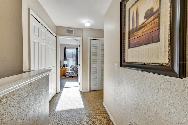 hallway featuring a textured wall, carpet flooring, baseboards, and visible vents