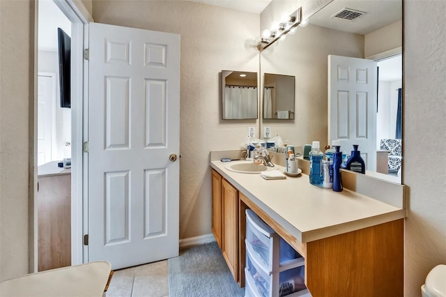 bathroom with tile patterned floors, visible vents, vanity, and a textured wall