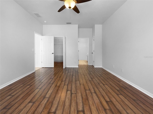 unfurnished bedroom with baseboards, dark wood-style floors, a closet, a walk in closet, and ceiling fan