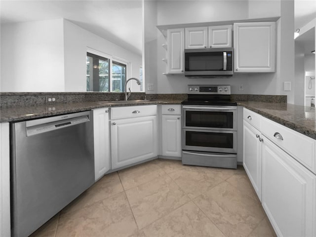 kitchen featuring appliances with stainless steel finishes, a sink, white cabinets, a peninsula, and dark stone counters