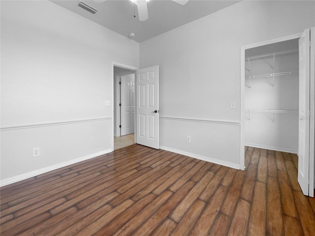 unfurnished bedroom featuring wood finished floors, a closet, a walk in closet, and baseboards