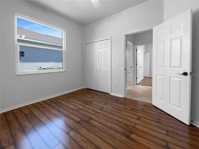 unfurnished bedroom featuring wood finished floors, baseboards, a closet, and a ceiling fan