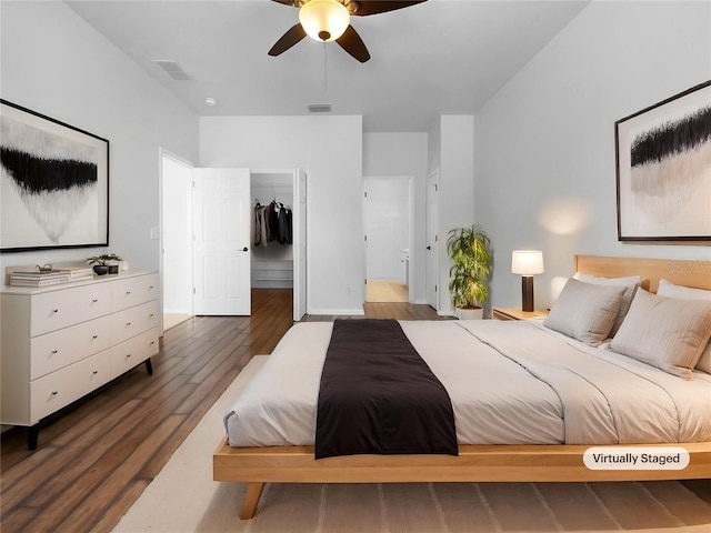 bedroom featuring wood finished floors, a walk in closet, ceiling fan, a closet, and baseboards