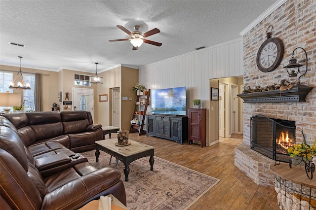 living room with ornamental molding, visible vents, wood-type flooring, ceiling fan with notable chandelier, and a fireplace