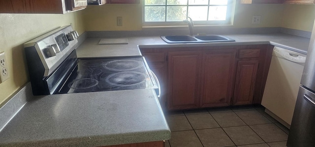 kitchen with a sink, brown cabinets, light tile patterned flooring, stainless steel electric range oven, and light countertops