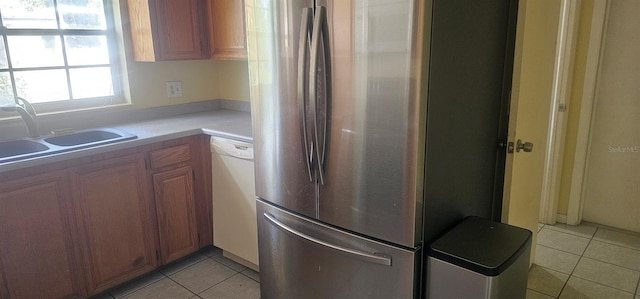 kitchen with freestanding refrigerator, light tile patterned floors, a sink, and dishwasher