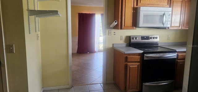 kitchen with stainless steel range with electric stovetop, light tile patterned floors, brown cabinets, white microwave, and light countertops