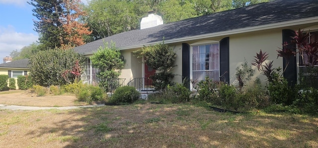 ranch-style house featuring roof with shingles, stucco siding, a front lawn, and a chimney