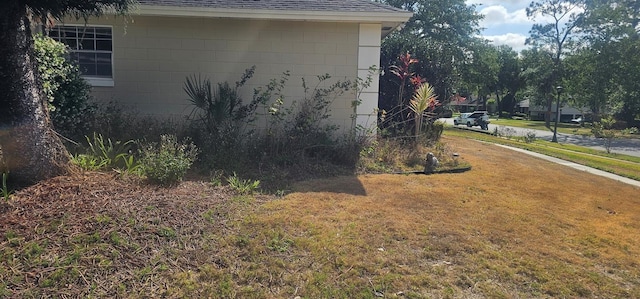 view of property exterior featuring roof with shingles, a lawn, and concrete block siding
