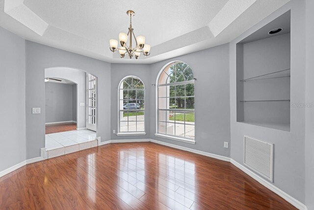 1802 Imperial Palm Dr, Apopka, FL 32712 - unfurnished dining area with arched walkways, wood finished floors, a chandelier, baseboards, and a tray ceiling
