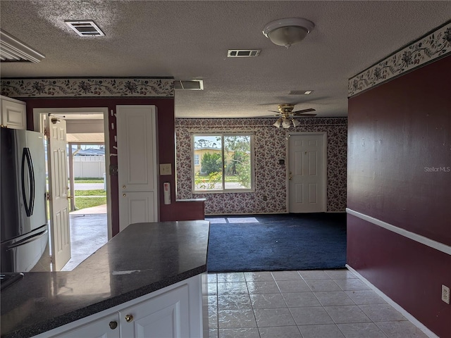 4299 Bullard St, North Port, FL 34287 - kitchen with freestanding refrigerator, wallpapered walls, light carpet, dark countertops, and white cabinets
