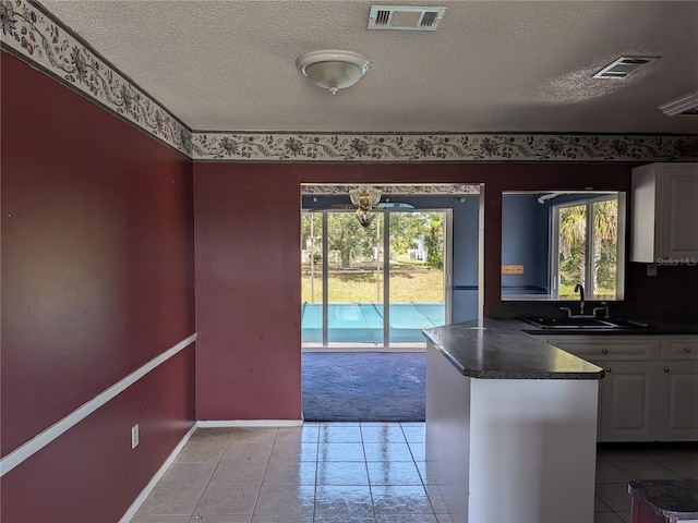 4299 Bullard St, North Port, FL 34287 - kitchen with dark countertops, a sink, white cabinets, light tile patterned floors, and a textured ceiling