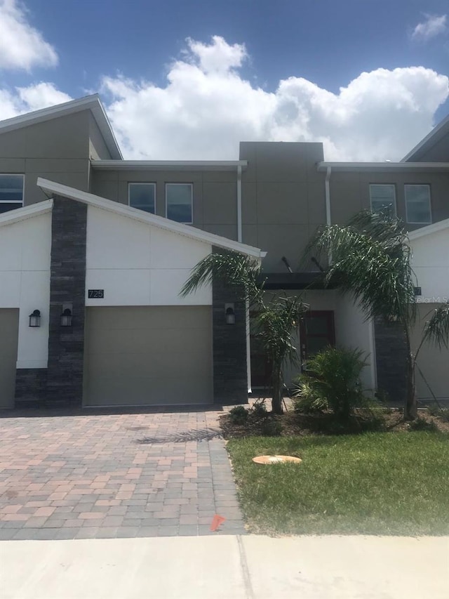 townhome / multi-family property featuring decorative driveway, a garage, and stucco siding