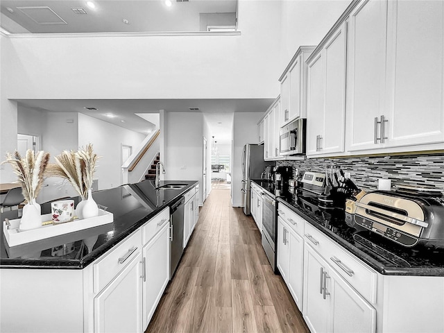 kitchen featuring appliances with stainless steel finishes, a sink, wood finished floors, tasteful backsplash, and a high ceiling