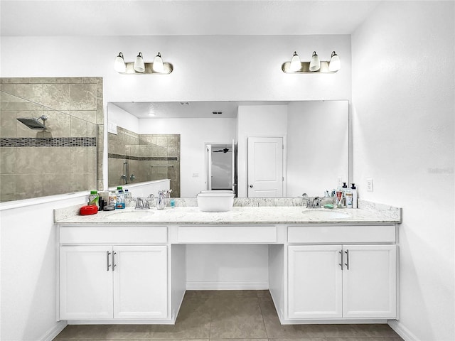 full bathroom with a tile shower, double vanity, tile patterned floors, and baseboards