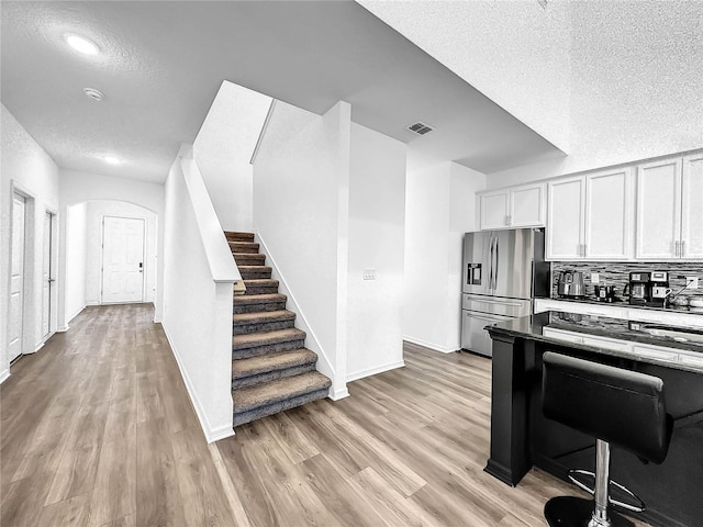 kitchen with stainless steel fridge, baseboards, light wood finished floors, a textured ceiling, and arched walkways