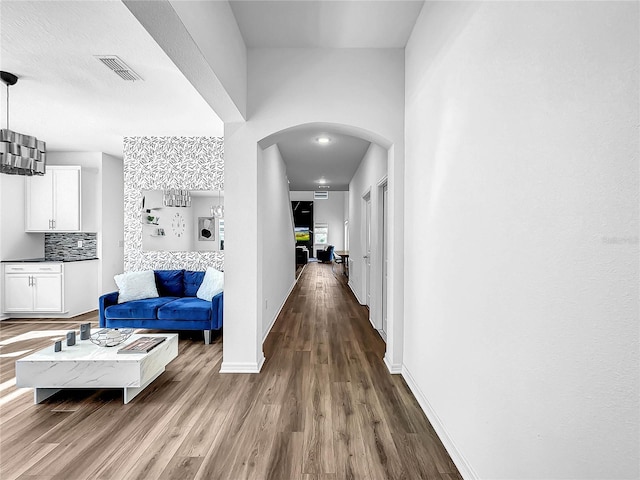 corridor featuring arched walkways, baseboards, visible vents, and wood finished floors