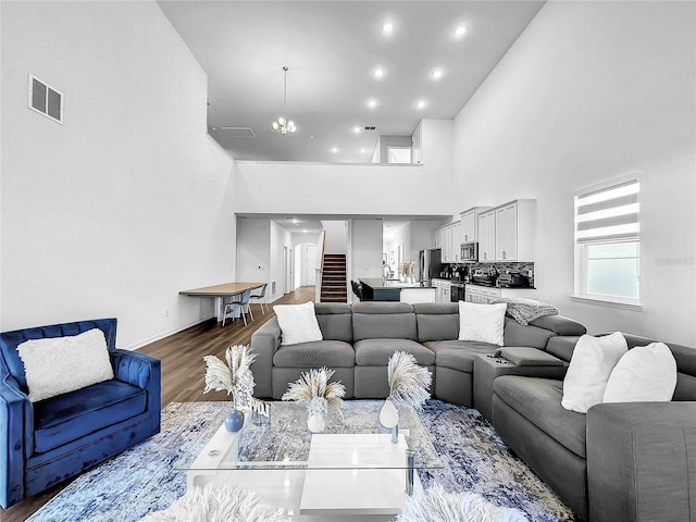 living area featuring a notable chandelier, baseboards, dark wood finished floors, visible vents, and a high ceiling