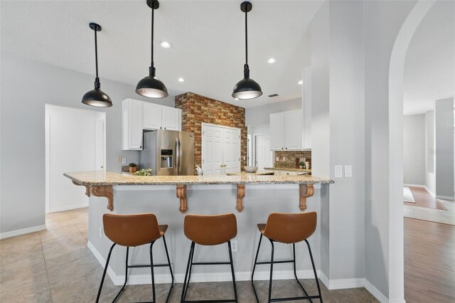 14848 Bonnybridge Dr, Orlando, FL 32826 - kitchen with stainless steel fridge, arched walkways, light stone countertops, white cabinetry, and a breakfast bar area