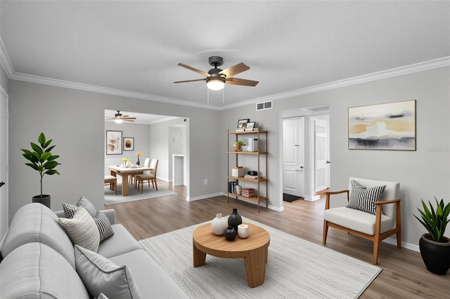 living area with a ceiling fan, wood finished floors, ornamental molding, and baseboards