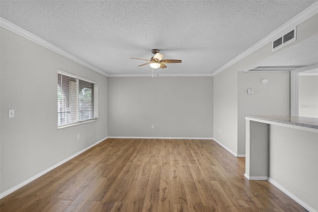 empty room with a textured ceiling, ceiling fan, wood finished floors, ornamental molding, and baseboards