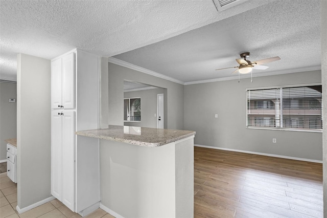kitchen featuring crown molding, white cabinets, a textured ceiling, ceiling fan, and light stone counters