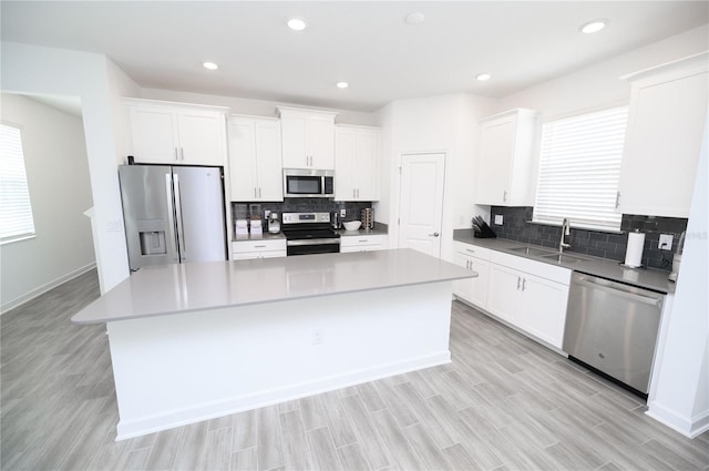 kitchen with stainless steel appliances, a sink, a kitchen island, backsplash, and white cabinetry