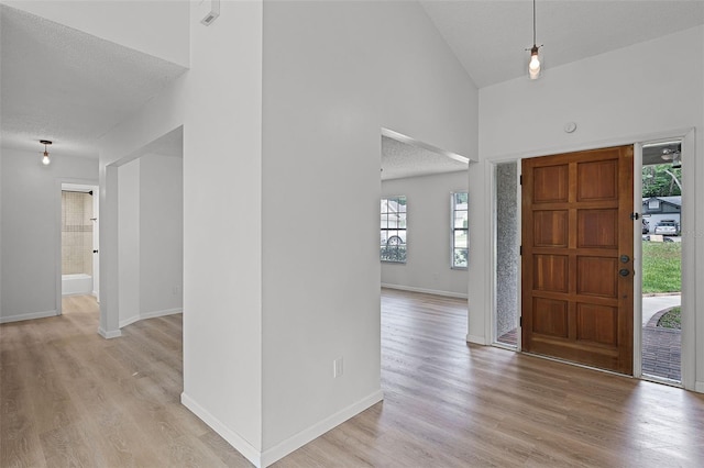 foyer featuring high vaulted ceiling, light wood finished floors, a textured ceiling, and baseboards