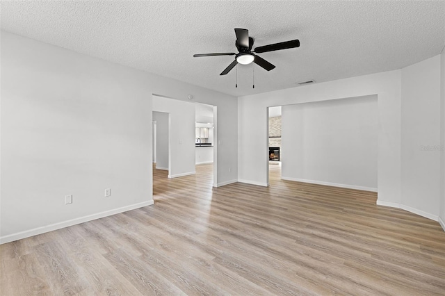 spare room with ceiling fan, a textured ceiling, light wood-type flooring, and baseboards
