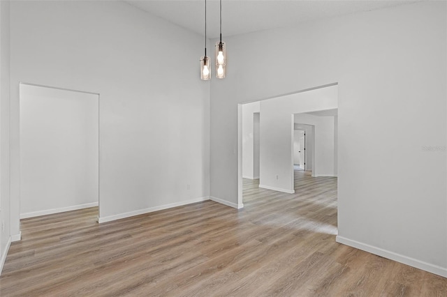 unfurnished dining area with a towering ceiling, light wood finished floors, baseboards, and a chandelier