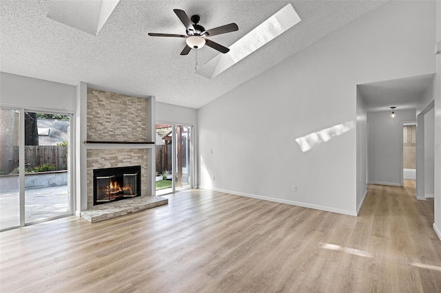 unfurnished living room with a textured ceiling, lofted ceiling, a ceiling fan, light wood-style flooring, and a large fireplace