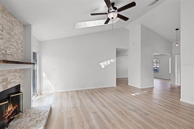 unfurnished living room with ceiling fan, a fireplace, wood finished floors, a skylight, and a textured ceiling