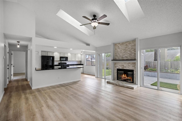 unfurnished living room featuring a skylight, a textured ceiling, a fireplace, a ceiling fan, and light wood-type flooring