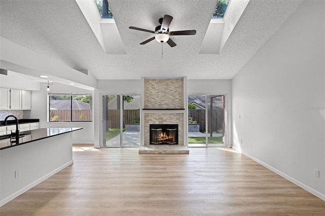unfurnished living room featuring a textured ceiling, a skylight, light wood-style flooring, and a fireplace