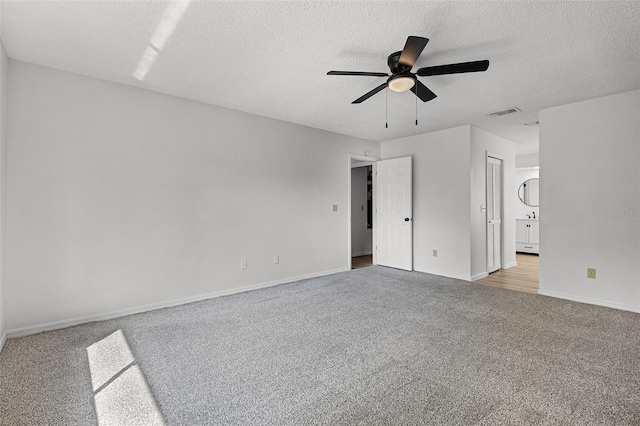 unfurnished bedroom with carpet floors, a textured ceiling, baseboards, ensuite bathroom, and ceiling fan