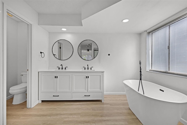 full bath featuring toilet, a freestanding tub, wood finished floors, baseboards, and recessed lighting
