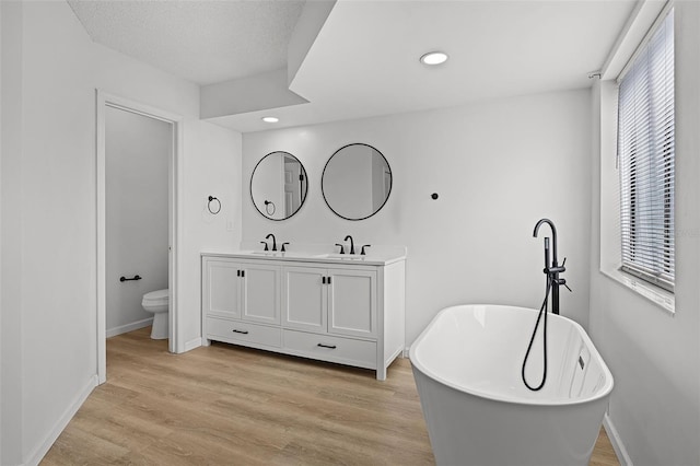 bathroom with toilet, double vanity, a freestanding bath, recessed lighting, and baseboards