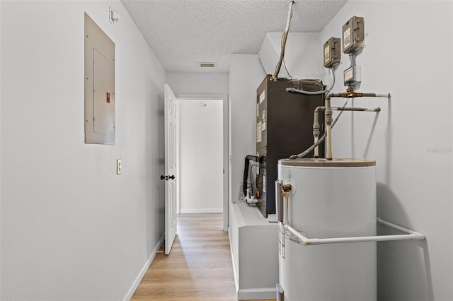 corridor with water heater, a textured ceiling, light wood finished floors, electric panel, and baseboards