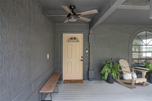 entrance to property featuring a ceiling fan and stucco siding