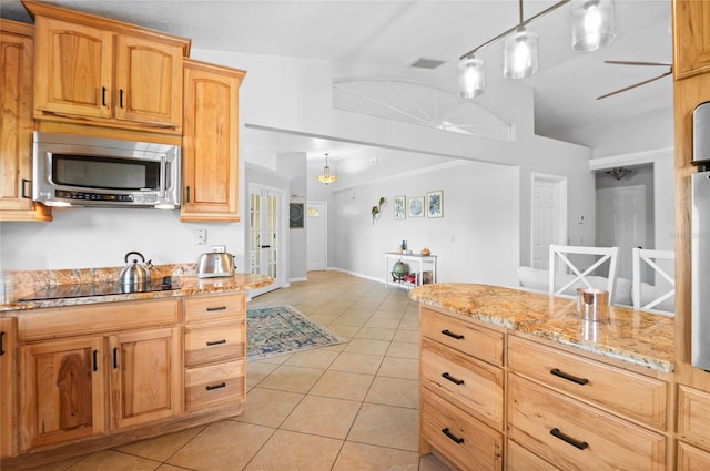 kitchen with stainless steel microwave, black electric stovetop, light tile patterned flooring, and light stone counters