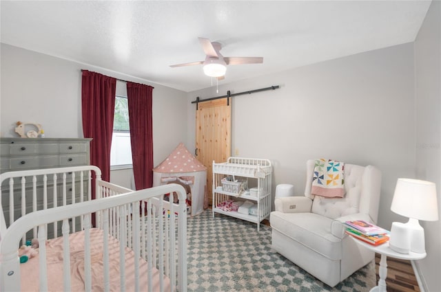 bedroom featuring a barn door, a crib, and a ceiling fan