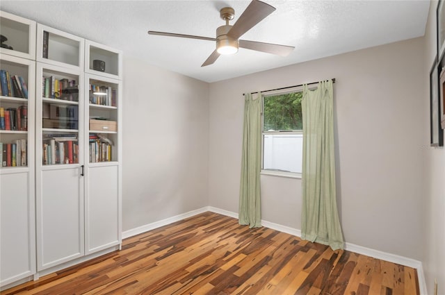 unfurnished room featuring ceiling fan, wood finished floors, baseboards, and a textured ceiling