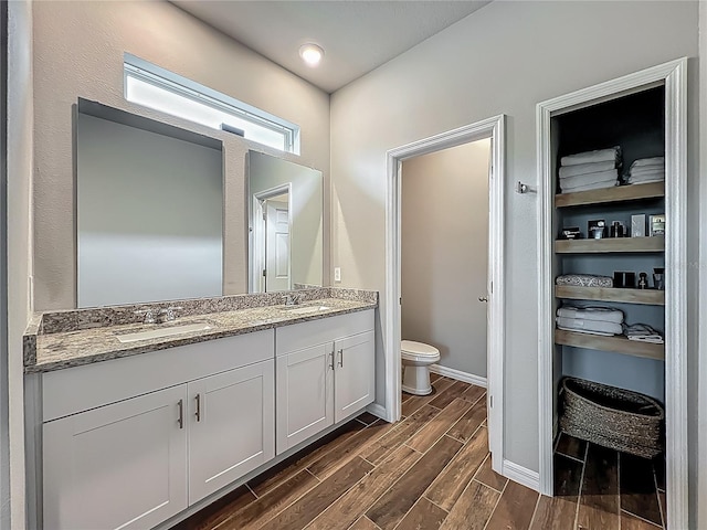 bathroom featuring wood finished floors, toilet, double vanity, and baseboards