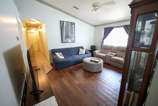 living area with crown molding, arched walkways, a ceiling fan, wood finished floors, and a textured ceiling
