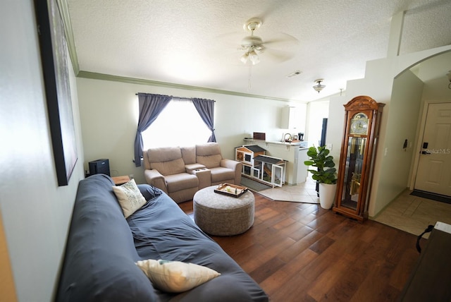 living room featuring arched walkways, ceiling fan, a textured ceiling, wood finished floors, and ornamental molding
